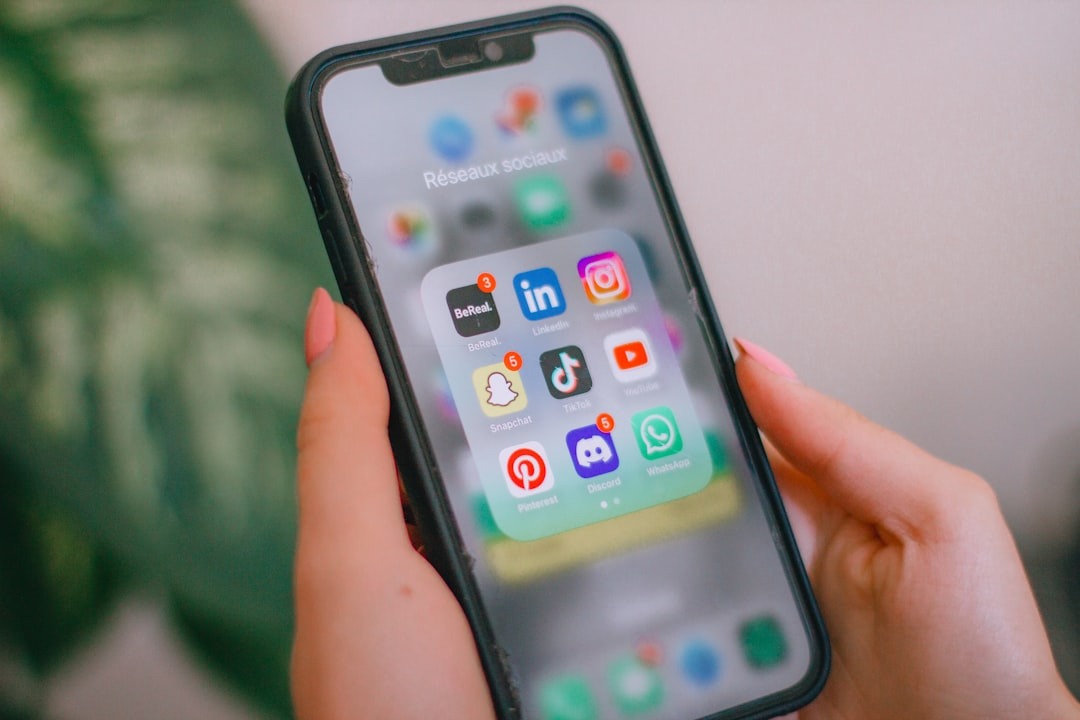 Hands with pink nails hold an iPhone displaying social media apps.